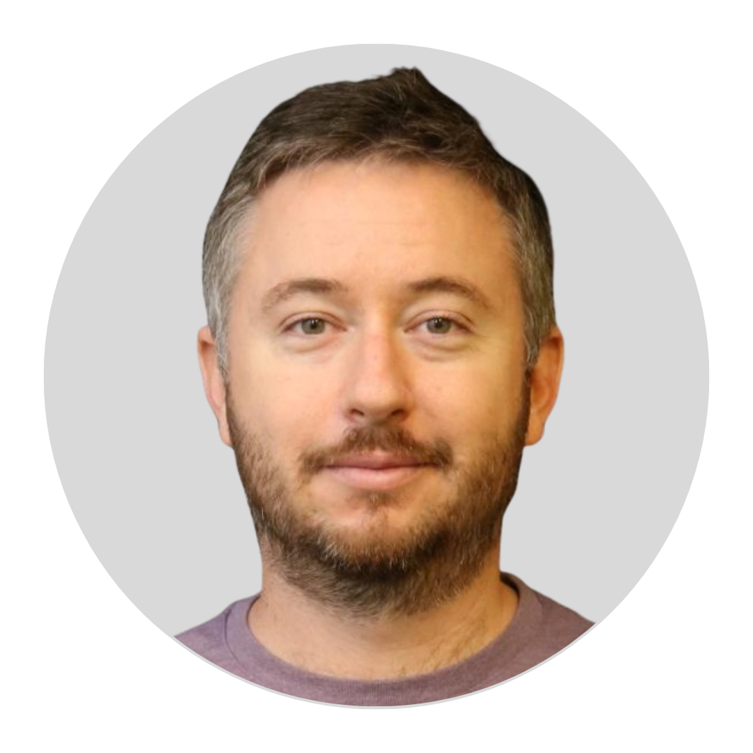 Bearded man with short brown hair in a purple shirt, shown in a circular portrait on a light gray background.