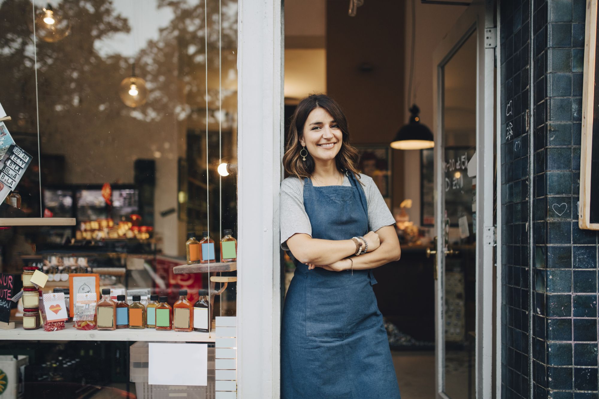 a woman wearing an apron leaning again a door frame of a business